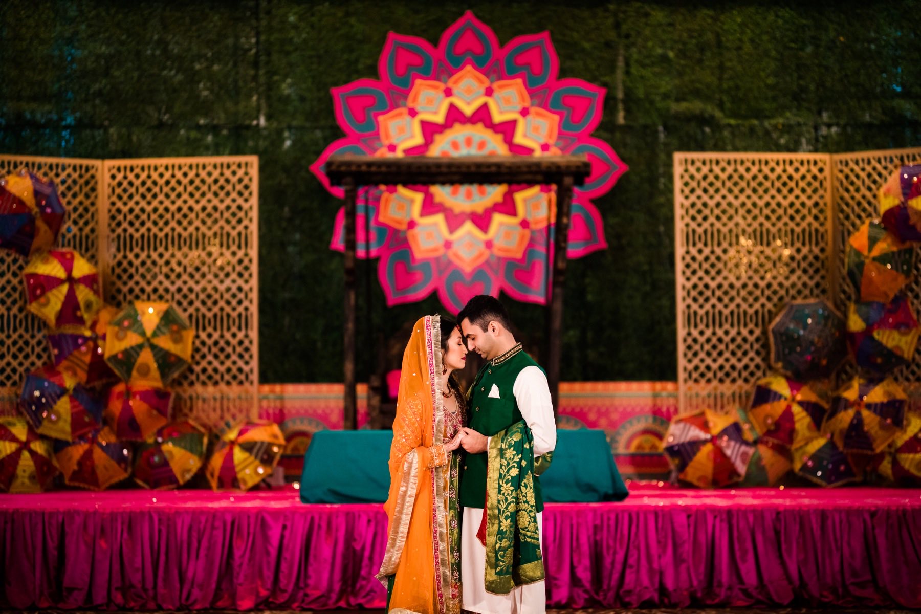 Couple standing close at vibrant mandala stage backdrop with colorful umbrellas and lanterns