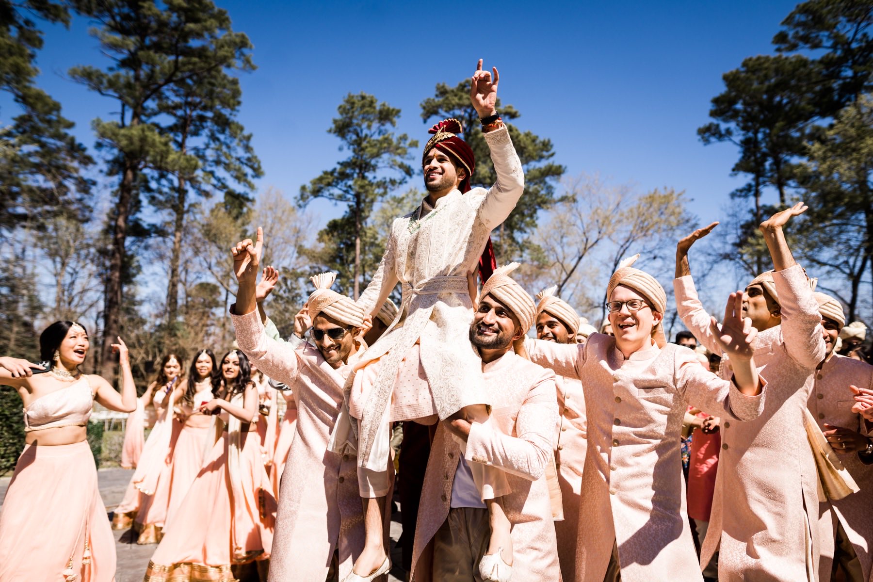 Groom lifted on shoulders by groomsmen celebrating at baraat under blue sky