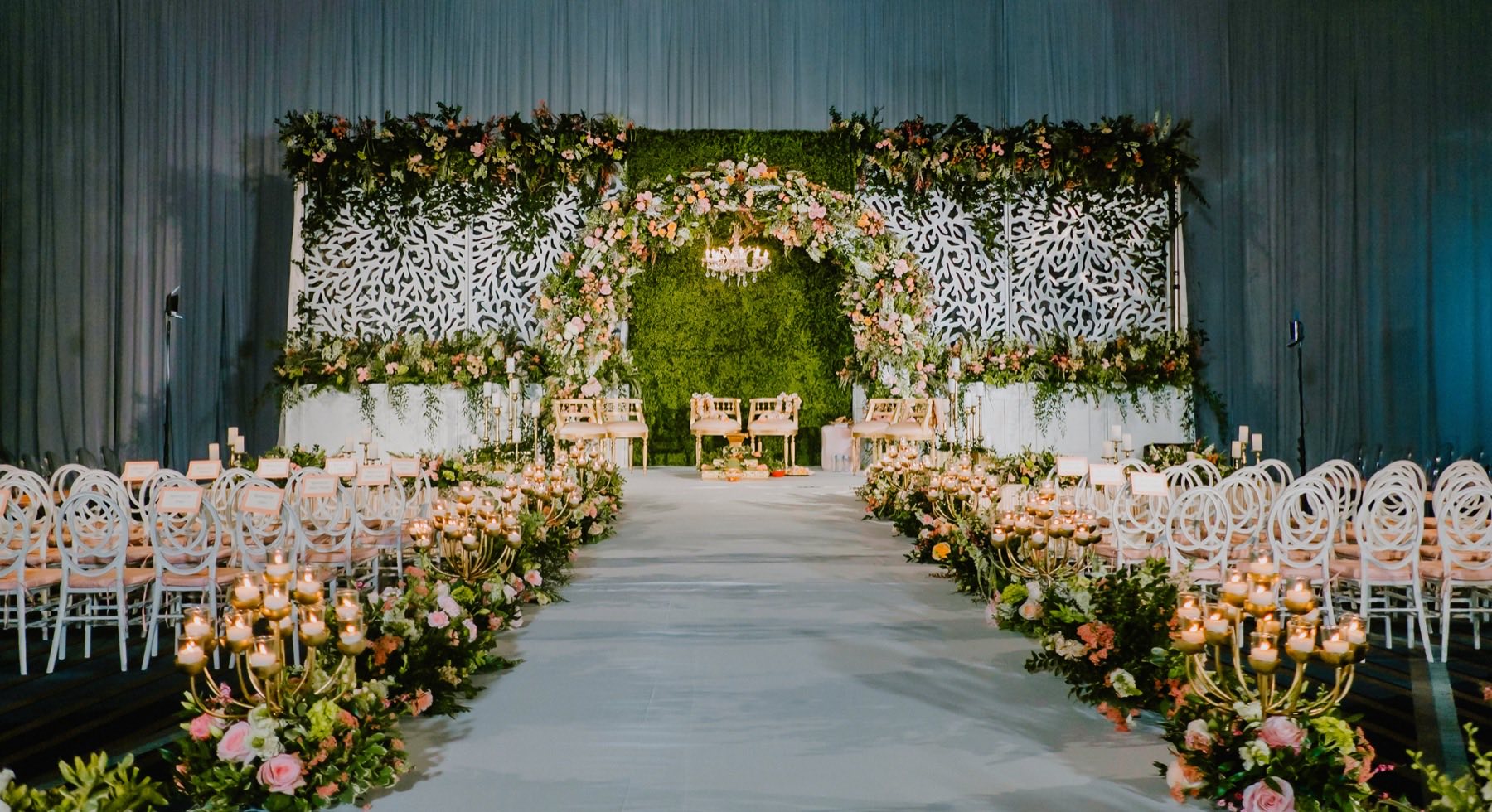 Ceremony aisle lined with gold candelabras beneath moss and floral arch