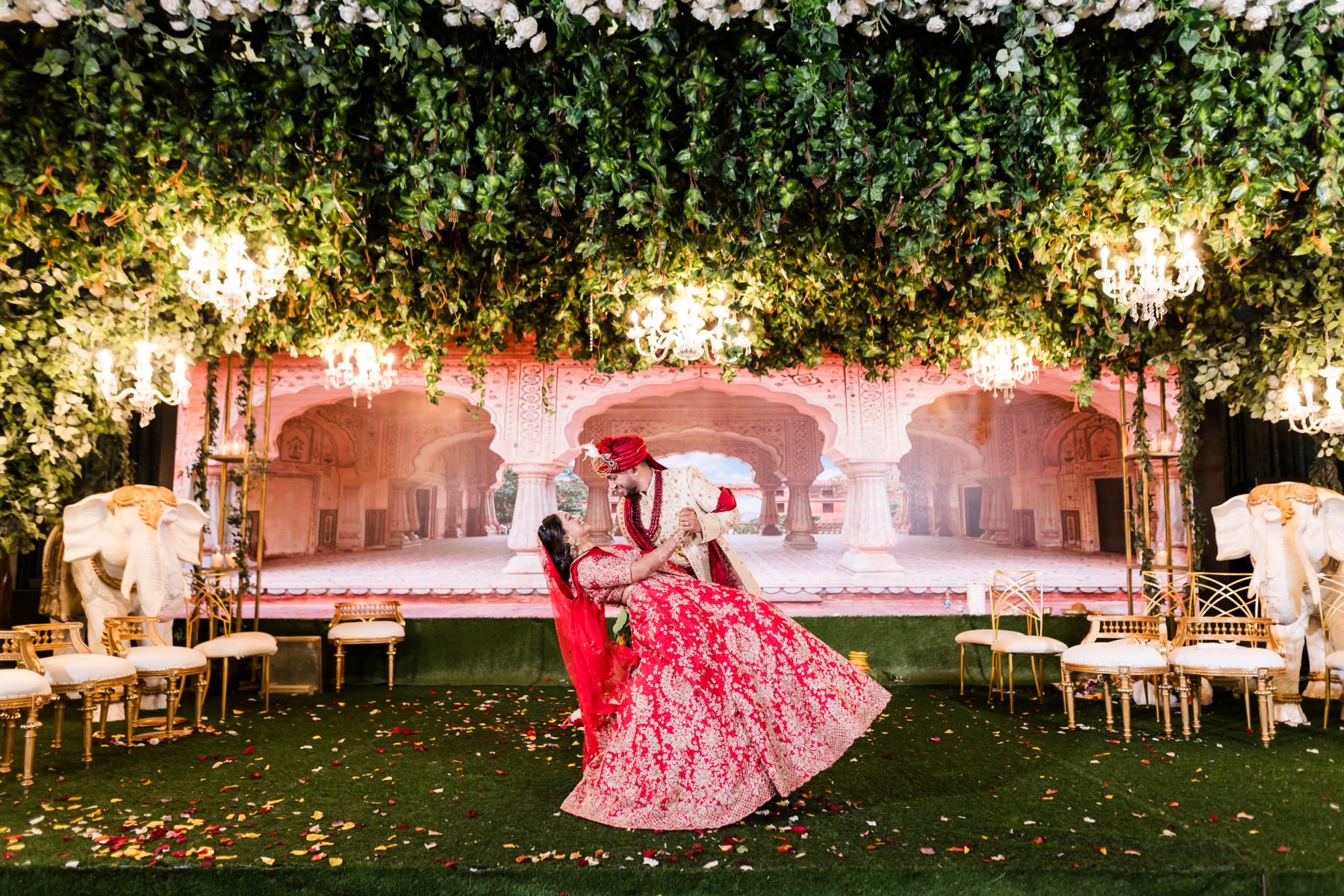 Couple dancing and dipping together beneath hanging chandeliers and green garland canopy