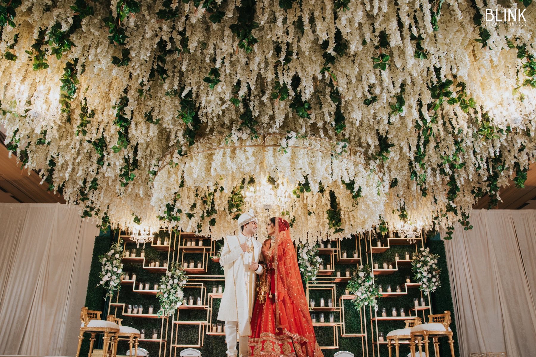 Couple standing beneath cascading white wisteria floral ceiling at ceremony