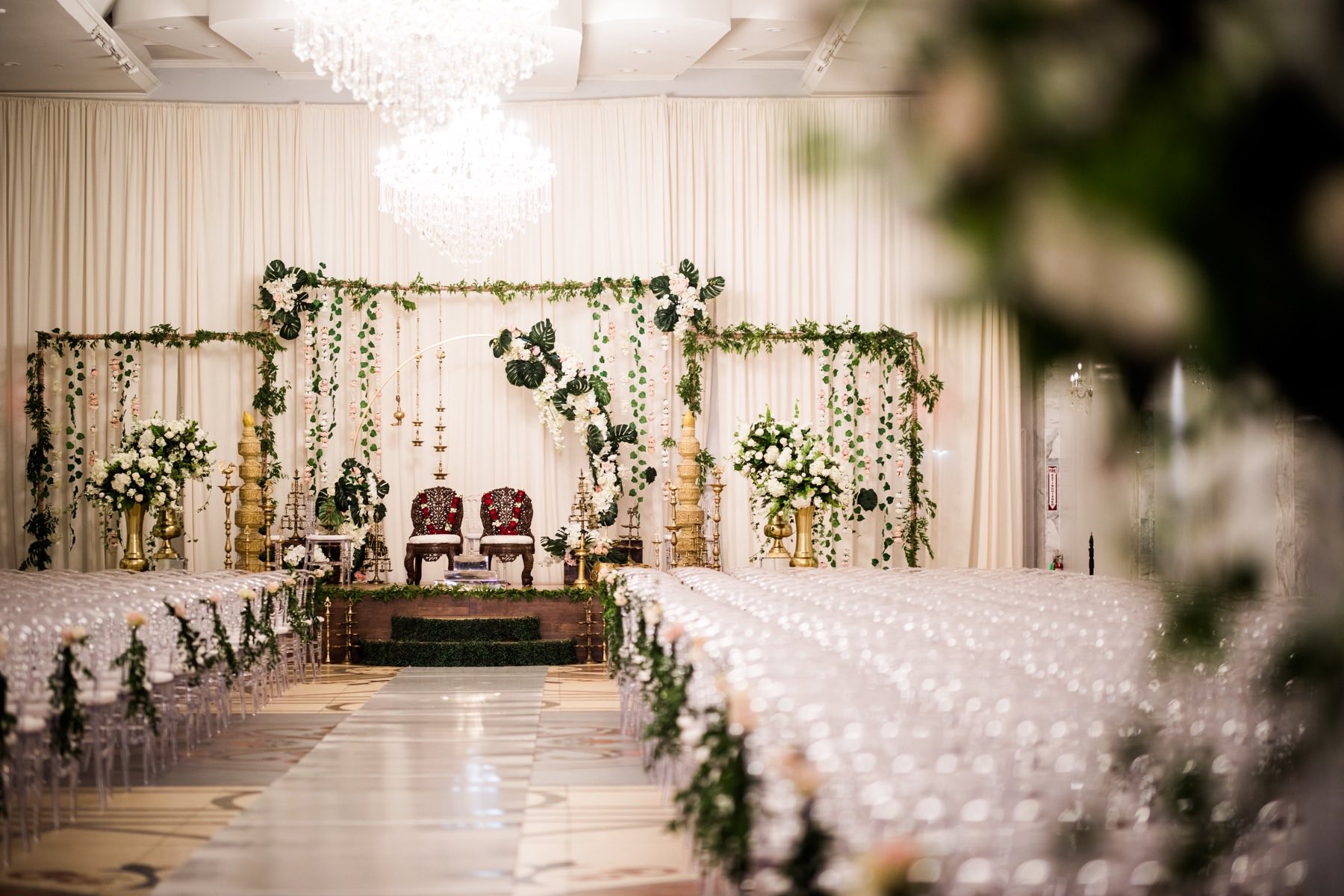 Indoor ceremony hall with tropical monstera leaf and white floral arch over the mandap