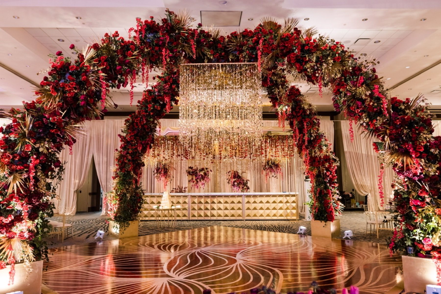 Grand reception entrance with dramatic red rose and gold floral arch and crystal chandelier