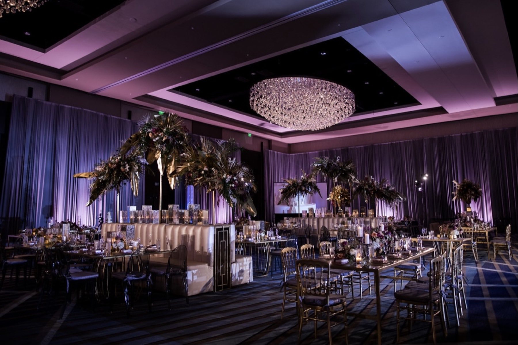 Dramatic purple-lit reception ballroom with tall gold palm leaf centerpieces and candles