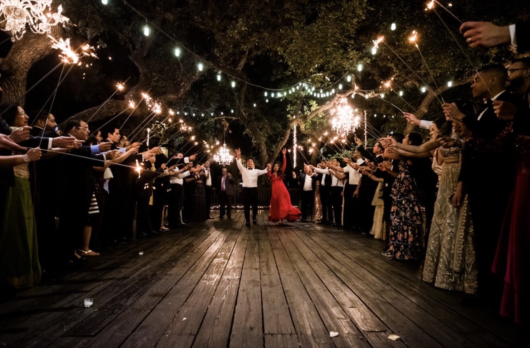 Couple walking through sparkler exit on wooden deck under string lights at night