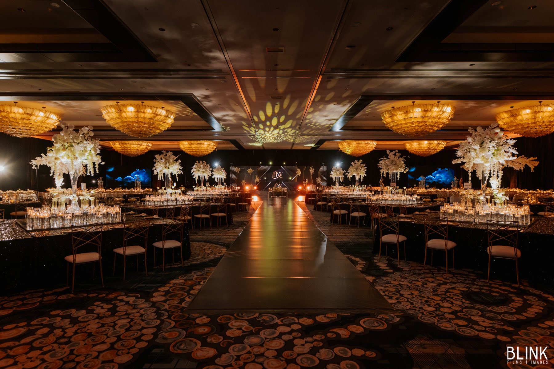 Elegant black and gold ballroom with white floral centerpieces and runway aisle