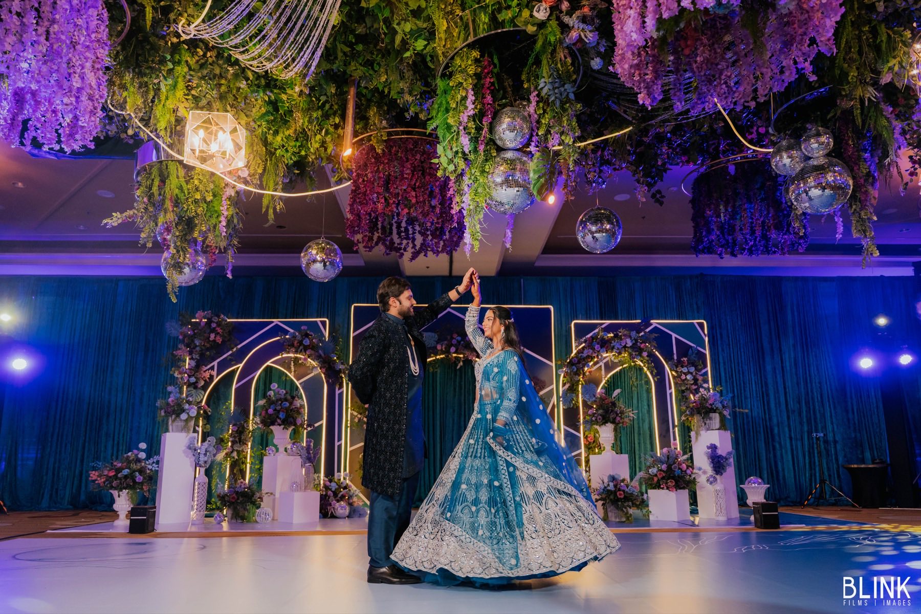Couple sharing first dance beneath wisteria ceiling with disco balls and blue lighting